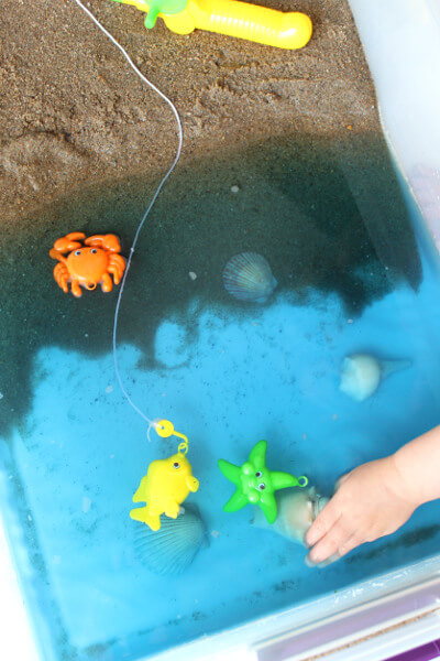 beach sensory bin with toys and toddler hands